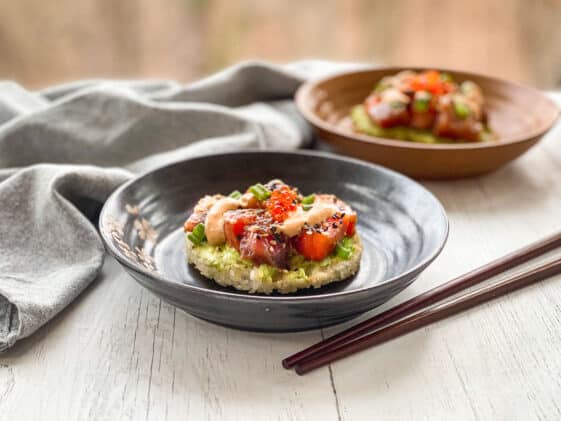 Sushi waffles with salmon and tuna on two round plates with a side of chopsticks on top of a white surface with a napkin in the background.