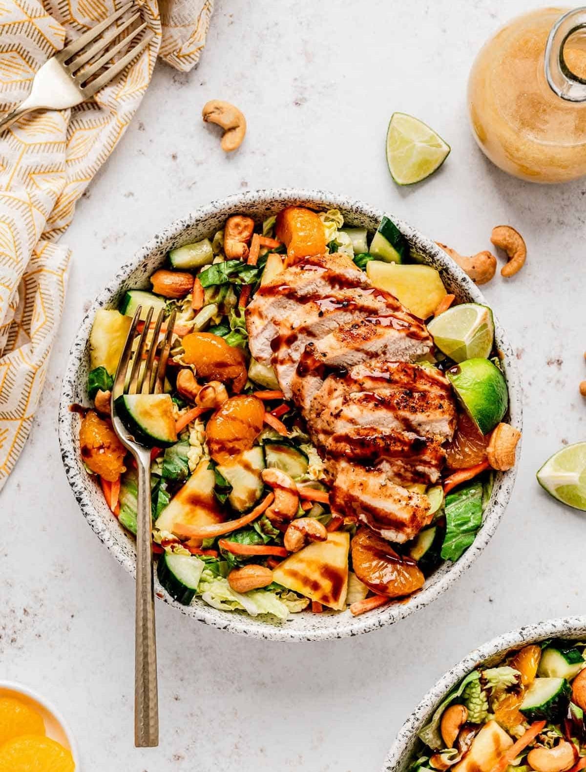 A Chinese cashew salad with grilled chicken and crisp vegetables in a round bowl with a fork on top and a napkin and dressing on the side.