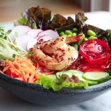 A grilled shrimp miso garden salad with fresh, colorful veggies in a round black bowl.